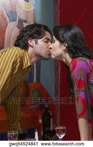 Stock Image - Side profile of a young couple kissing each other in a restaurant. Fotosearch
