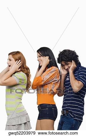 Side profile of a young man and two young women standing with their fingers in their ears View Large Photo Image Stock Photo - Side profile of a young man and two young women standing with their fingers in their ears. Fotosearch
