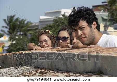 Stock Image - Side profile of a young man with three young women looking over a castle wall, Morro Castle, Old San Juan, San Juan, Puerto Rico. Fotosearch