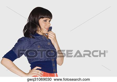 Stock Image - Side profile of a young woman holding her collar and smiling. Fotosearch