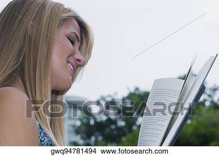 Side profile of a young woman reading a book and smiling View Large Photo Image Picture - Side profile of a young woman reading a book and smiling. Fotosearch