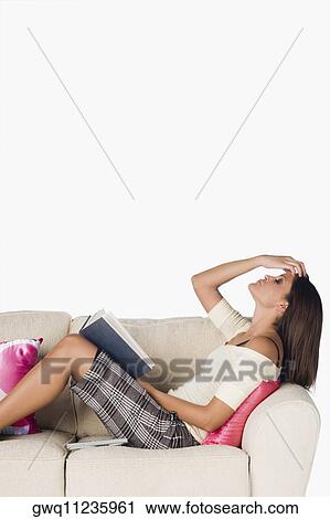 Side profile of a young woman reclining on a couch and holding a book View Large Photo Image Stock Image - Side profile of a young woman reclining on a couch and holding a book. Fotosearch