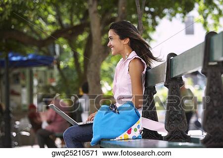 Stock Image - Side profile of a young woman sitting on a bench and using a laptop, Old San Juan, San Juan, Puerto Rico. Fotosearch