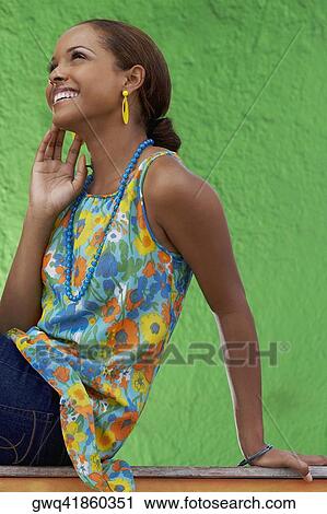 Stock Image - Side profile of a young woman sitting on a railing and smiling. Fotosearch