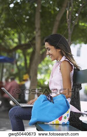 Side profile of a young woman sitting on a bench and using a laptop, Old San Juan, San Juan, Puerto Rico View Large Photo Image Stock Image - Side profile of a young woman sitting on a bench and using a laptop, Old San Juan, San Juan, Puerto Rico. Fotosearch