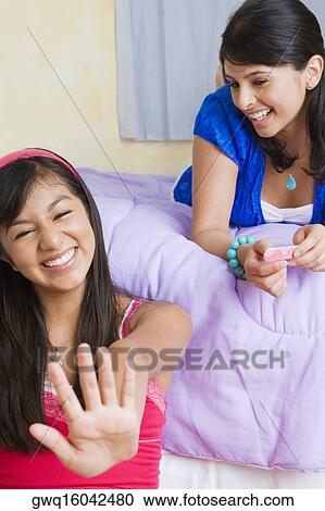 Teenage girl looking at polished nails and a young woman lying on the bed behind her View Large Photo Image Stock Image - Teenage girl looking at polished nails and a young woman lying on the bed behind her. Fotosearch