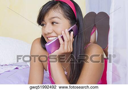 Stock Image - Teenage girl lying on the bed and talking on a mobile phone. Fotosearch
