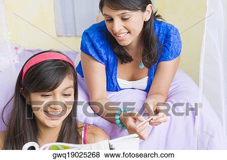 Teenage girl reading a magazine with a young woman lying on the bed behind her View Large Photo Image Stock Photo - Teenage girl reading a magazine with a young woman lying on the bed behind her. Fotosearch