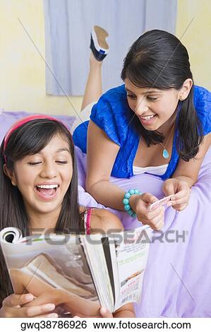 Teenage girl reading a magazine with a young woman lying on the bed behind her View Large Photo Image Stock Photograph - Teenage girl reading a magazine with a young woman lying on the bed behind her. Fotosearch