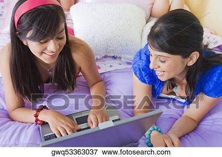 Teenage girl working on a laptop with a young woman lying beside her on the bed View Large Photo Image Stock Photo - Teenage girl working on a laptop with a young woman lying beside her on the bed. Fotosearch