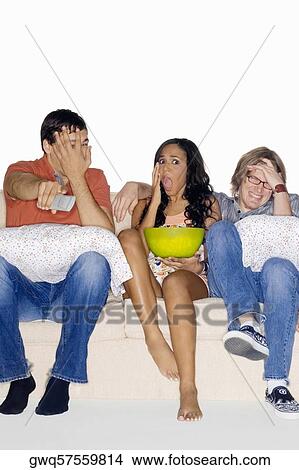 Three friends sitting on a couch and watching television View Large Photo Image Picture - Three friends sitting on a couch and watching television. Fotosearch