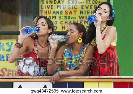 Stock Photography - Three young women leaning on a railing and drinking water from bottles. Fotosearch