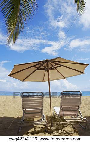 Stock Photograph - Two outdoor chairs and a beach umbrella on the beach, Ocean Park, El Condado, San Juan, Puerto Rico. Fotosearch
