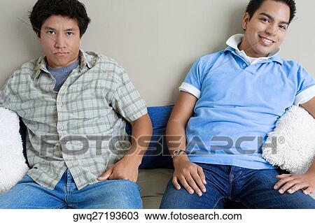 Two young men sitting on a couch View Large Photo Image Stock Image - Two young men sitting on a couch. Fotosearch