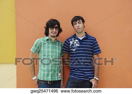 Two young men standing in front of a wall View Large Photo Image Stock Photograph - Two young men standing in front of a wall. Fotosearch