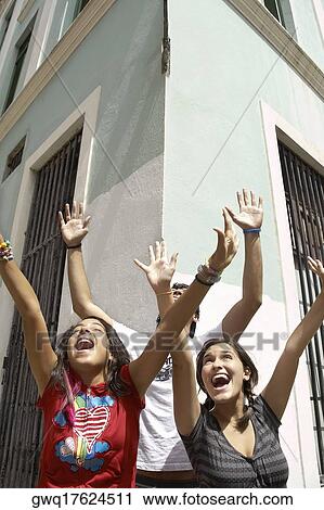 Stock Image - Two young women and a young man standing together with their arms raised and laughing. Fotosearch