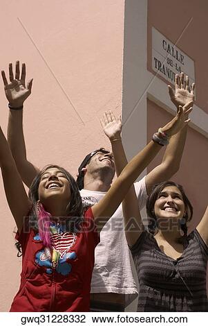 Two young women and a young man standing together with their arms raised and smiling View Large Photo Image Stock Image - Two young women and a young man standing together with their arms raised and smiling. Fotosearch