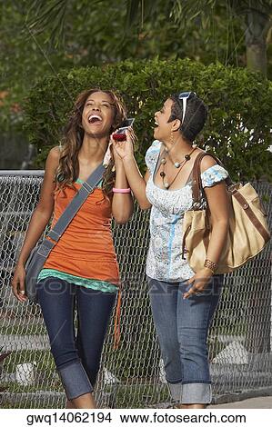 Picture - Two young women holding a mobile phone and laughing. Fotosearch