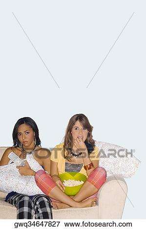 Two young women sitting on a couch and watching television View Large Photo Image Stock Photo - Two young women sitting on a couch and watching television. Fotosearch