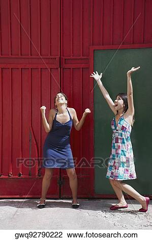 Two young women standing with their arms raised and smiling View Large Photo Image Stock Image - Two young women standing with their arms raised and smiling. Fotosearch