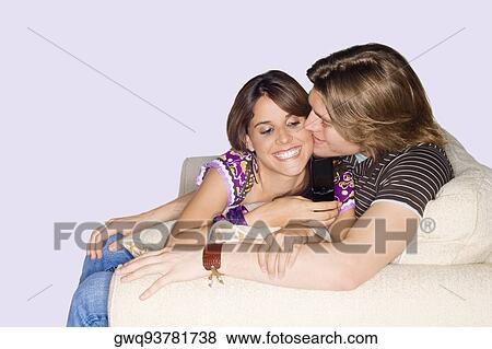 Young man kissing a young woman using a mobile phone View Large Photo Image Stock Photo - Young man kissing a young woman using a mobile phone. Fotosearch