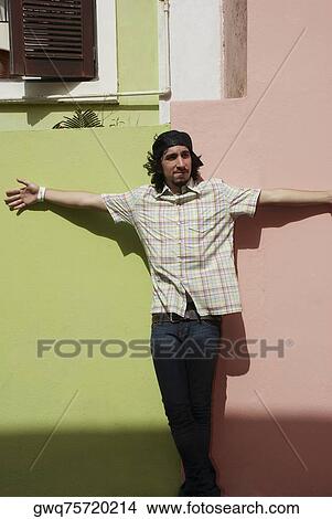 Picture - Young man leaning against a wall with his arms outstretched. Fotosearch