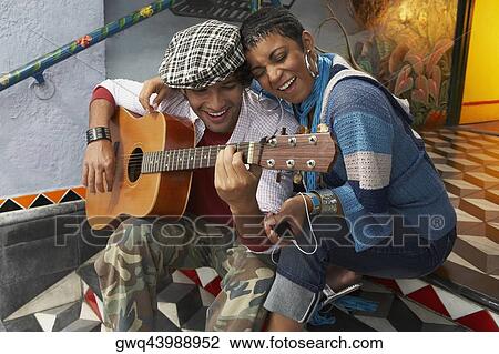 Young man playing a guitar and smiling with a young woman View Large Photo Image Stock Image - Young man playing a guitar and smiling with a young woman. Fotosearch
