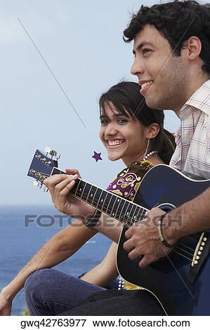 Young man sitting with a young woman and playing a guitar View Large Photo Image Stock Photo - Young man sitting with a young woman and playing a guitar. Fotosearch