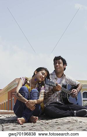 Young man sitting with a young woman and playing a guitar View Large Photo Image Stock Photo - Young man sitting with a young woman and playing a guitar. Fotosearch