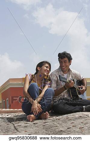 Stock Photo - Young man sitting with a young woman and playing a guitar. Fotosearch