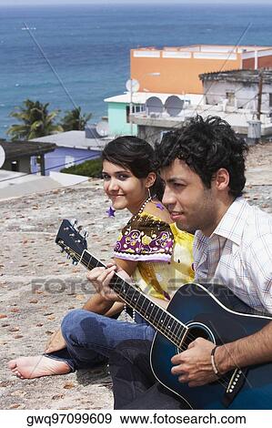 Young man sitting with a young woman and playing a guitar View Large Photo Image Stock Photo - Young man sitting with a young woman and playing a guitar. Fotosearch