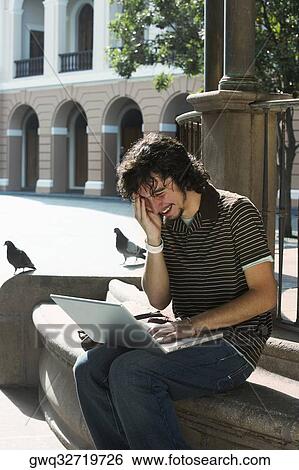 Stock Photograph - Young man using a laptop and laughing. Fotosearch