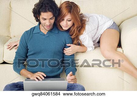 Young man using a laptop with a young woman leaning over him View Large Photo Image Picture - Young man using a laptop with a young woman leaning over him. Fotosearch
