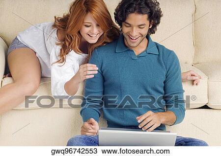 Young man using a laptop with a young woman leaning over him View Large Photo Image Stock Image - Young man using a laptop with a young woman leaning over him. Fotosearch