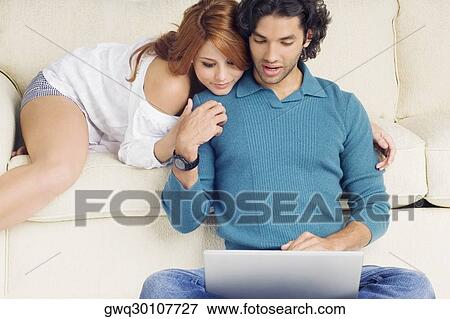 Stock Photo - Young man using a laptop with a young woman leaning over him. Fotosearch