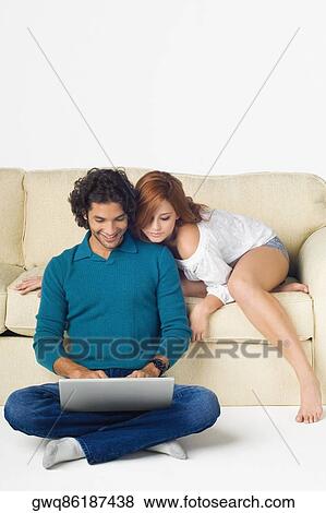 Young man using a laptop with a young woman leaning over him View Large Photo Image Stock Photo - Young man using a laptop with a young woman leaning over him. Fotosearch