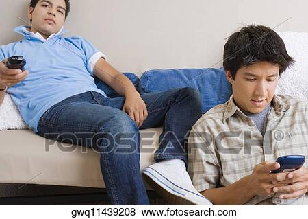 Young man using a mobile phone while another young man operating a remote control View Large Photo Image Stock Photo - Young man using a mobile phone while another young man operating a remote control. Fotosearch