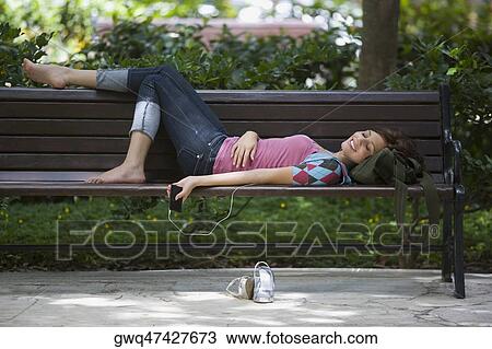 Young woman listening to an MP3 player and lying on a bench View Large Photo Image Stock Image - Young woman listening to an MP3 player and lying on a bench. Fotosearch