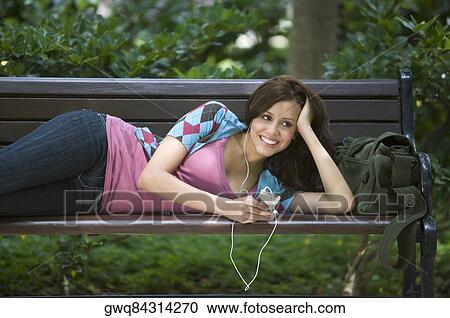 Young woman listening to an MP3 player and lying on a bench View Large Photo Image Stock Image - Young woman listening to an MP3 player and lying on a bench. Fotosearch