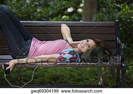 Young woman listening to an MP3 player and lying on a bench View Large Photo Image Stock Photo - Young woman listening to an MP3 player and lying on a bench. Fotosearch