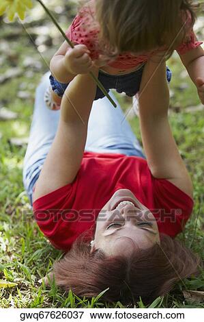 Young woman lying on grass and picking up her daughter View Large Photo Image Stock Photo - Young woman lying on grass and picking up her daughter. Fotosearch