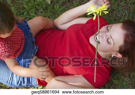 Young woman lying on grass with her daughter sitting on her stomach View Large Photo Image Picture - Young woman lying on grass with her daughter sitting on her stomach. Fotosearch