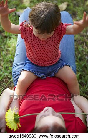 Young woman lying on grass with her daughter sitting on her stomach View Large Photo Image Stock Image - Young woman lying on grass with her daughter sitting on her stomach. Fotosearch
