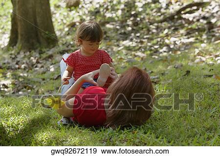 Stock Photo - Young woman lying on grass with her daughter sitting on her stomach. Fotosearch