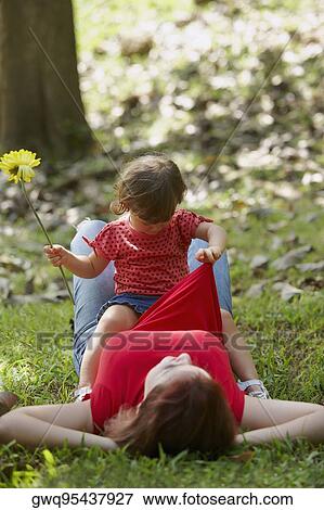 Young woman lying on grass with her daughter sitting on her stomach View Large Photo Image Stock Photo - Young woman lying on grass with her daughter sitting on her stomach. Fotosearch