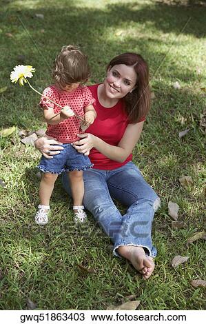 Stock Image - Young woman sitting on grass with her daughter and smiling. Fotosearch