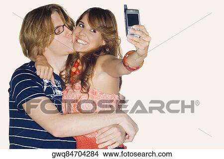 Young woman taking a photograph of herself with a young man kissing her View Large Photo Image Picture - Young woman taking a photograph of herself with a young man kissing her. Fotosearch