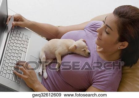 Young woman using a laptop and a puppy lying on her View Large Photo Image Stock Photo - Young woman using a laptop and a puppy lying on her. Fotosearch
