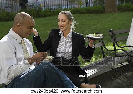 Businessman and a businesswoman having food on a park bench View Large Photo Image Stock Image - Businessman and a businesswoman having food on a park bench. Fotosearch