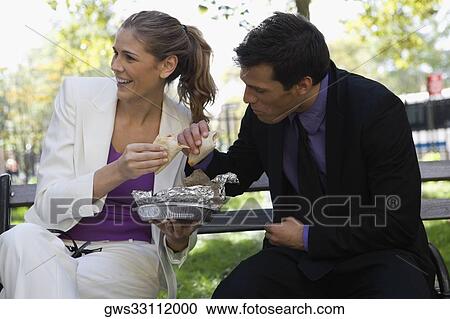 Businessman and a businesswoman having food on a park bench View Large Photo Image Stock Image - Businessman and a businesswoman having food on a park bench. Fotosearch